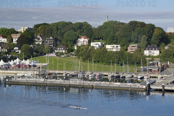 Houses and boats along a waterfront promenade with trees and green areas under a blue sky, Kiel Fjord, Holtanau, Kiel, Schleswig-Holstein, Germany