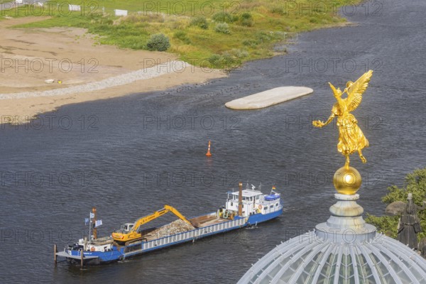 View from the lantern of the Church of Our Lady. Fama (the goddess of rumours) on the dome of the Academy of Fine Arts, with the pillar foundations of the former Carola bridges. The dredger Domarin straightens the fairway for shipping, Dresden, Saxony, Germany