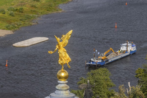 View from the lantern of the Church of Our Lady. Fama (the goddess of rumours) on the dome of the Academy of Fine Arts, with the pillar foundations of the former Carola bridges. The dredger Domarin straightens the fairway for shipping, Dresden, Saxony, Germany