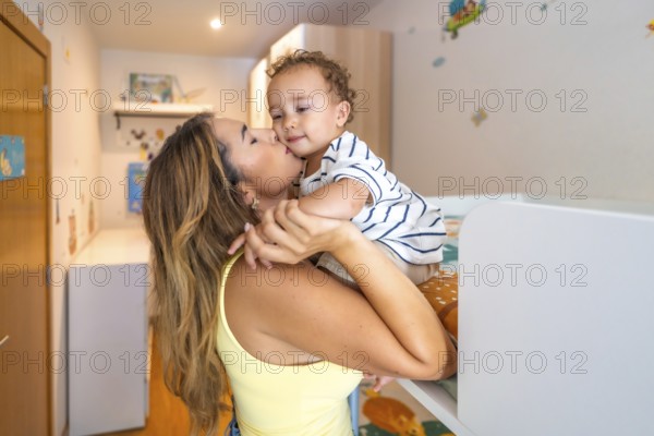 Mom kissing her baby boy in a decorated bedroom, showing love and affection in a cozy home environment