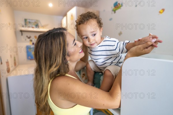 Smiling mother holding hands with her baby son while playing in a decorated children's bedroom
