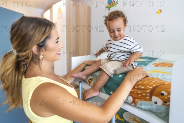 Young mother assisting her little son as he carefully climbs down from a bunk bed in a beautifully decorated children's bedroom