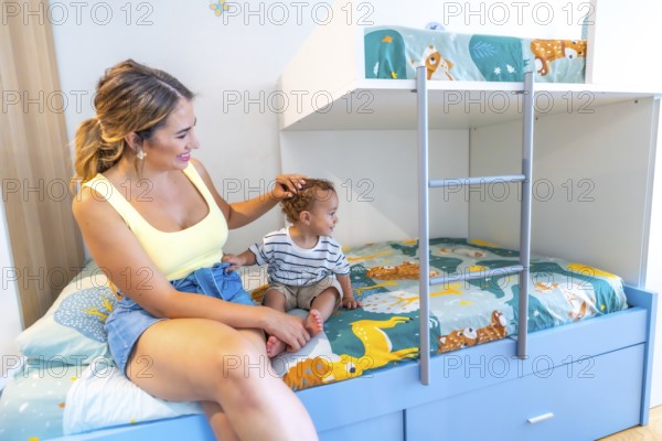 Mom gently caressing her little son while sitting together on a bunk bed in a brightly colored bedroom