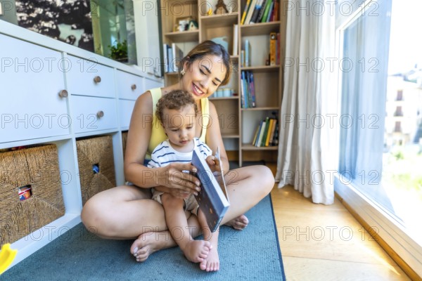 Happy mother and her little son reading a book together, sitting on the floor in the living room