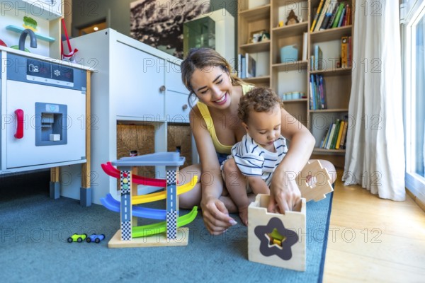 Smiling mother and her baby boy having fun together while playing with educational toys on the floor in a cozy playroom