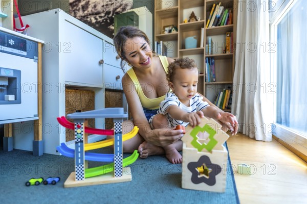 Happy mother and her cute son are playing together with colorful educational toys in a modern playroom