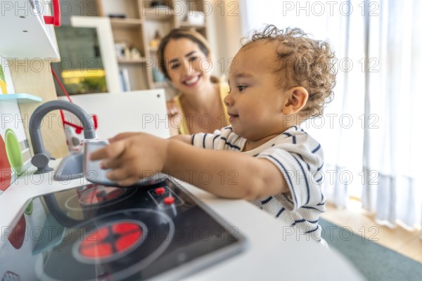 Happy toddler playing with toy kitchen while his mother watches him, promoting early childhood development and imaginative play