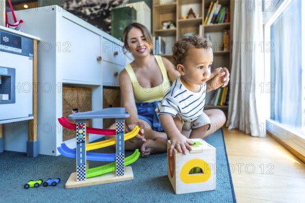 Happy mother watching her toddler son playing with educational wooden toys in a modern living room