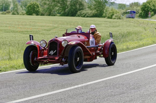 A red classic car drives on a country road through a green landscape, classic car, car race, Mille Miglia, 1000 Miglia, 2015, Tuscany, Rome Lake Garda, Italy