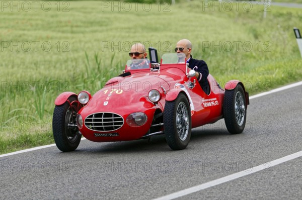 An open red sports car with two drivers drives through a green landscape, classic car, car race, Mille Miglia, 1000 Miglia, 2015, Tuscany, Rome Lake Garda, Italy