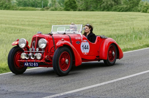 A red vintage car drives with two people through a green landscape, classic car, car race, Mille Miglia, 1000 Miglia, 2015, Tuscany, Rome Lake Garda, Italy