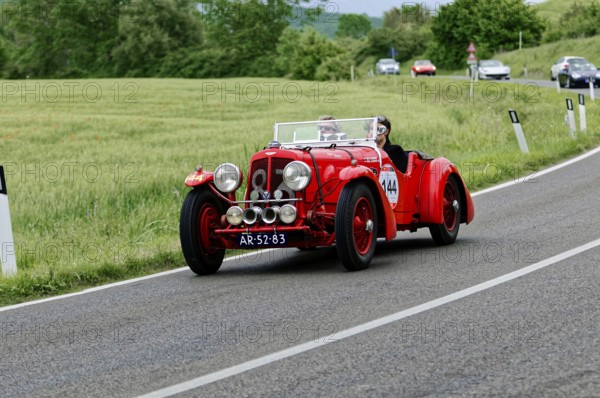 A red classic car with two drivers enjoys a drive in a picturesque landscape, classic car, car race, Mille Miglia, 1000 Miglia, 2015, Tuscany, Rome Lake Garda, Italy