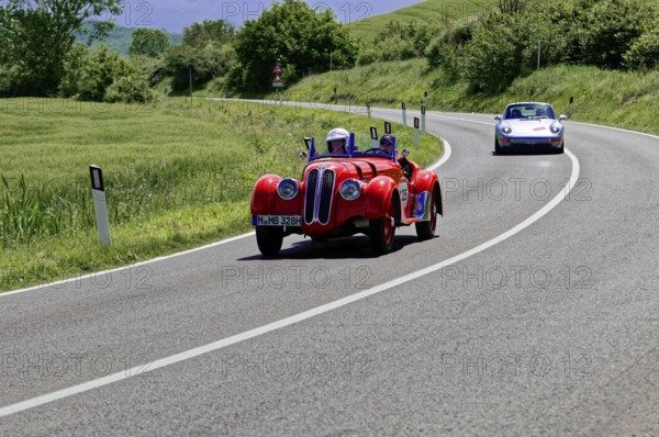 A sporty red vintage car followed by a modern vehicle on a road, vintage car, car race, Mille Miglia, 1000 Miglia, 2015, Tuscany, Rome Lake Garda, Italy