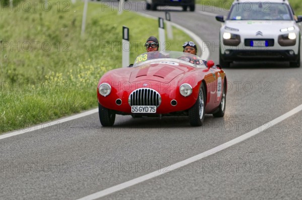 A red vintage racing car drives along green fields on a winding country road during a rally, vintage car, car race, Mille Miglia, 1000 Miglia, 2015, Tuscany, Rome Lake Garda, Italy