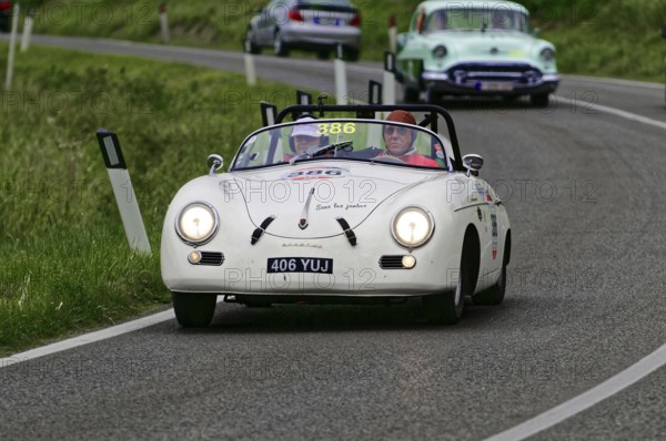 A white Porsche convertible with two occupants drives on a winding country road in front of a green car, classic car, car race, Mille Miglia, 1000 Miglia, 2015, Tuscany, Rome Lake Garda, Italy