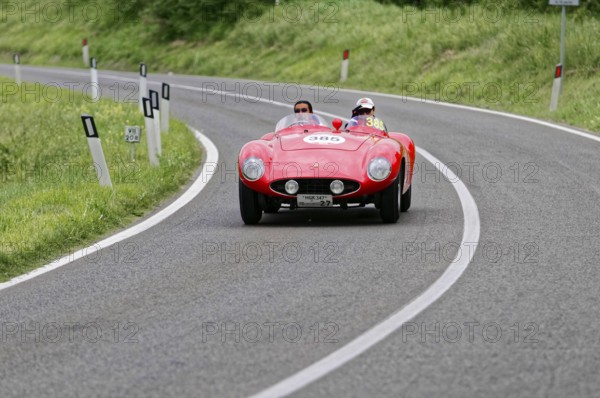A red vintage convertible car with two occupants drives fast on a tarmac road, vintage car, car race, Mille Miglia, 1000 Miglia, 2015, Tuscany, Rome Lake Garda, Italy