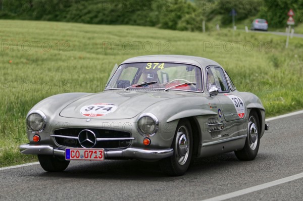 A silver Mercedes vintage car with racing stickers drives on a road in natural surroundings, vintage car, car racing, Mille Miglia, 1000 Miglia, 2015, Tuscany, Rome Lake Garda, Italy