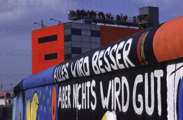 Berlin, DEU, 18.10.1998 -- Site at Potsdamer Platz. Listed remnant of the Berlin Wall painted by artists: Everything is getting better but nothing is going to be good! In the background, visitors on the infobox viewing platform. (art, culture, architecture, tourism)