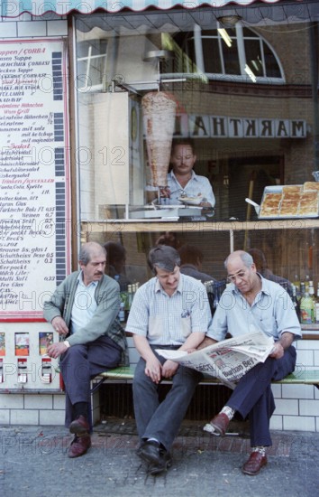 Berlin, DEU, 10.06.1998 -- Turkish men sit reading newspapers in front of a kebab shop. (Free time, street scene)