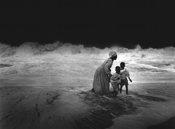 NGA, Lagos, 20.05.97 -- Free churches in Lagos. -- The waves of the Atlantic ocean wash around members of a free church on Victoria Island off Lagos. Christian groups in the 12 million metropolis have created a refuge on the beach for their religious practice. Many have been pushed to the beach following the settlement of foreign companies and are trying to organize their lives here.