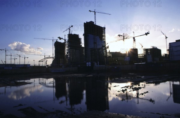 Berlin, DEU, 26.10.1998 -- Silhouette of the construction site on Potsdamer Platz at sunset. Reflection in a puddle. (construction crane, water)