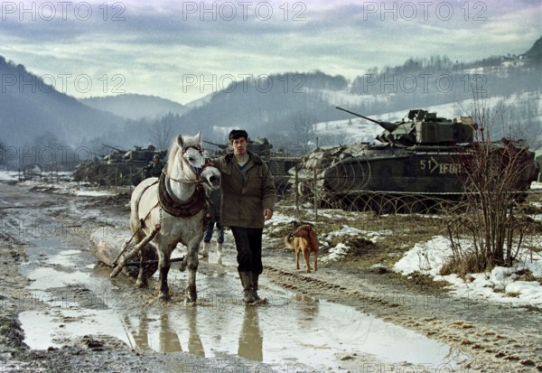 BIH, Tuzla, 01.01.1996 -- A Bosnian farmer pulls his horse past the base camp of American IFOR soldiers. -- A farmer passes a compound of U.S. IFOR troops in the mountains near Tuzla, as the American advance team deploys.   Bosnia Hercogovina, Eastern Europe