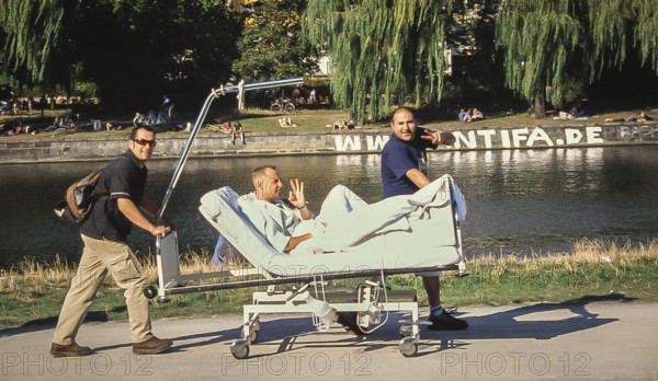 DEU Germany Germany Berlin Two men drive their friend on a hospital bed along the Landwehr Canal near the Urban Hospital on a sunny summer day