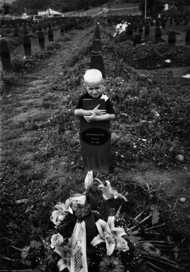 BIH, Bosnia, Screbrenica, 10.07.2005, A boy hugs a Muslim grave cross