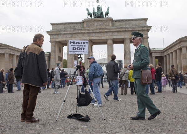 DEU Germany Berlin fundraisers in GDR uniform with a state border sign. The Lord collects donations for a children's foundation in the Dominican Republic and hands out day visas for a small fee. Scene on the eve of the 20th anniversary of German reunification on the festival mile in Berlin. Germany Berlin Man in GDR uniform collects donations in front of the Brandenburg Gate. Scene from the public party one day ahead of the celebration marking the 20th anniversary of the German reunification