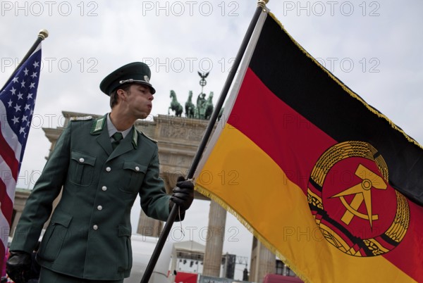 DEU Germany Berlin Actor wearing NVA uniform blows the GDR flag. Scene on the eve of the 20th anniversary of German reunification on the festival mile in Berlin. Germany Berlin Actor in GDR Army uniform blows towards the GDR flag. Scene from the public party one day ahead of the celebration marking the 20th anniversary of the German reunification