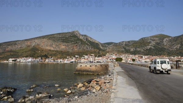 An off-road vehicle on a coastal road with a view of a city and mountains, Monemvasia, Monemvassia, Malvasy, Byzantine small town, rocky island, fortress, Laconia, Peloponnese, peninsula, Greece