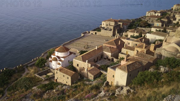 Drone shot, Holy Church of the Virgin Mary Chrysaphitissa, historic coastal village with church and dome, surrounded by traditional architecture, Monemvasia, Monemvassia, Malvasy, Byzantine small town, rocky island, fortress, Laconia, Peloponnese, peninsula, Greece