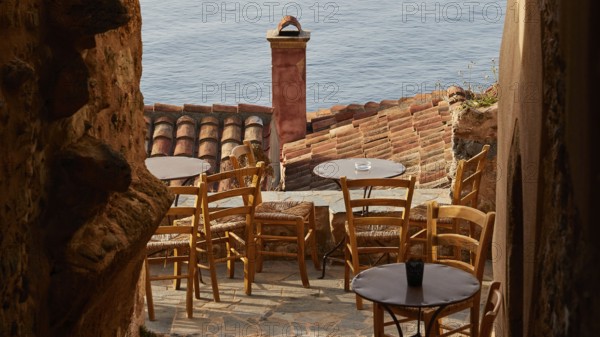 Soft morning light, narrow alley with café terrace and view of the blue sea through tiled roofs, Monemvasia, Monemvassia, Malvasy, Byzantine small town, rocky island, fortress, Laconia, Peloponnese, peninsula, Greece