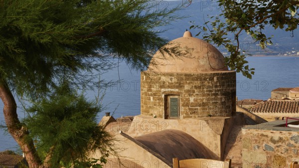 Soft morning light, view over a dome and the sea, framed by green trees and tiled roofs, Monemvasia, Monemvassia, Malvasy, small Byzantine town, rocky island, fortress, Laconia, Peloponnese, peninsula, Greece