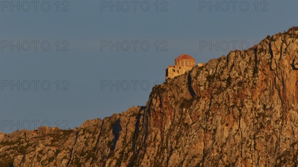 Orhodox church of Hagia Sophia, chapel high on a rock, illuminated in orange evening light, Monemvassia, Malvasy, Byzantine small town, rocky island, fortress, Laconia, Peloponnese, peninsula, Greece