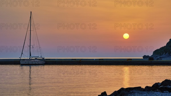 Sailing boat against orange sky and calm sea at sunrise, Monemvasia, Monemvassia, Malvasy, Byzantine small town, rocky island, fortress, Laconia, Peloponnese, peninsula, Greece