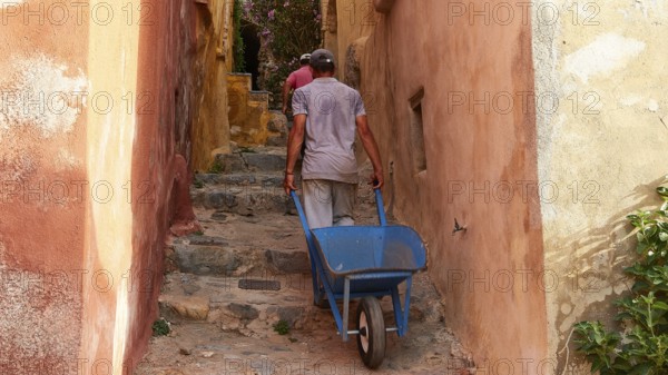 A man pulls a wheelbarrow up a narrow, colorful alley, Monemvassia, Malvasy, small Byzantine town, rocky island, fortress, Laconia, Peloponnese, peninsula, Greece