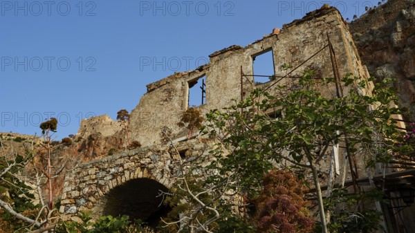 Dilapidated stone structure nestled in lush vegetation under clear skies, Monemvasia, Monemvassia, Malvasy, Byzantine small town, rocky island, fortress, Laconia, Peloponnese, peninsula, Greece