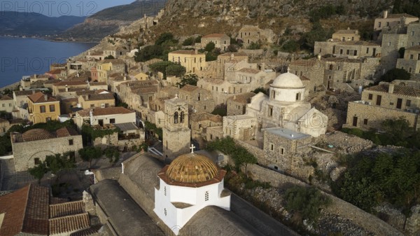 Drone shot, panoramic view of the seaside village with distinctive church dome and ancient architecture, Holy Church of the Virgin Mary Myrtidiotissa (or Critikias), Holy Church of Christ in Chains, Elkomenos Christos, Monemvasia, Monemvassia, Malvasy, Byzantine small town, rocky island, fortress, Laconia, Peloponnese, peninsula, Greece