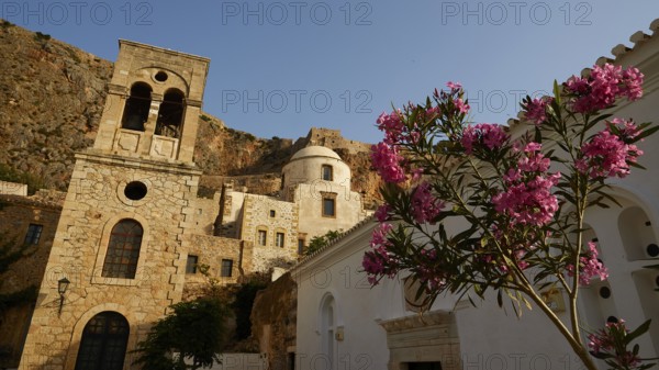 Soft morning light, Holy Church of Christ in Chains, Elkomenos Christos, Blooming oleanders in front of a historic building and a church under clear sky, Monemvasia, Monemvassia, Malvasy, Byzantine small town, rocky island, fortress, Laconia, Peloponnese, peninsula, Greece