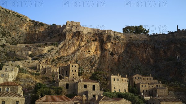 Drone shot, medieval buildings on a rocky cliff overlooking the Mediterranean Sea at sunset, Monemvasia, Monemvassia, Malvasy, Byzantine small town, rocky island, fortress, Laconia, Peloponnese, peninsula, Greece