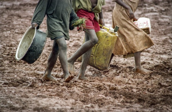 TZA Tanzania scene in the Benaco Camp refugee camp, to which up to 500, 000 Rwandan Tutsis fled the genocide in their country. Refugee children walk barefoot through muddy paths to arrange water and food. TZA Tanzania Scene at the Benaco Camp, where an estimate of 500, 000 Rwandan Tutsi refugees fled the genocide in their country. Refugee Kids Walks Barfoot Through Muddy Pathes to Organise Water and Food