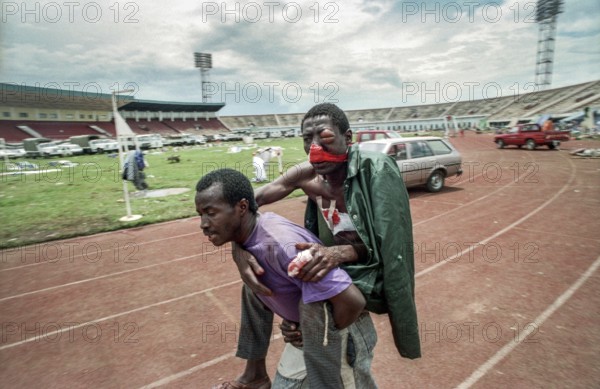 RWA Rwanda Kigali An injured Tutsi refugee who fled to the sports stadium is carried by a man to a Red Cross injury collection center. The stadium had previously been attacked with mortar shells by Hutu rebels. RWA Rwanda Kigali An injured Tutsi refugee who escaped the massacre is carried to the Red Cross Logistic. The Man Is Part of Tutsis Group Who Were Attacked by Hutu Rebels as They Were Hiding in Kigali's Main Sport Stadium