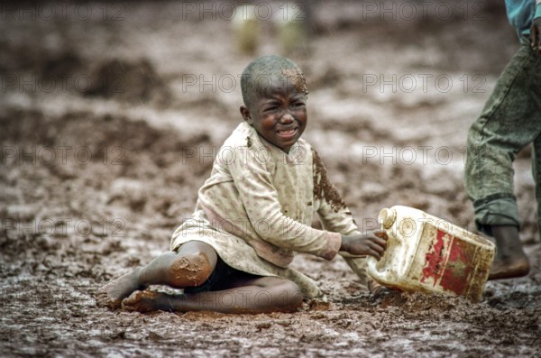 TZA Tanzania scene in the Benaco Camp refugee camp, to which up to 500, 000 Rwandan Tutsis fled the genocide in their country. A refugee child has gone off on a muddy path. TZA Tanzania Scene at the Benaco Camp, where an estimate of 500, 000 Rwandan Tutsi refugees fled the genocide in their country. A Refugee Kid, Send for Water Supply, Sliped on a Muddy Path