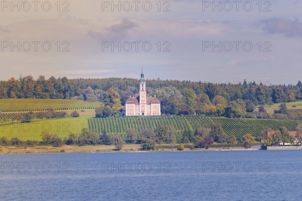 A church on a hill surrounded by vineyards and forest, with a view of a lake under a colorful autumn sky, Birnau, Lake Constance, Germany