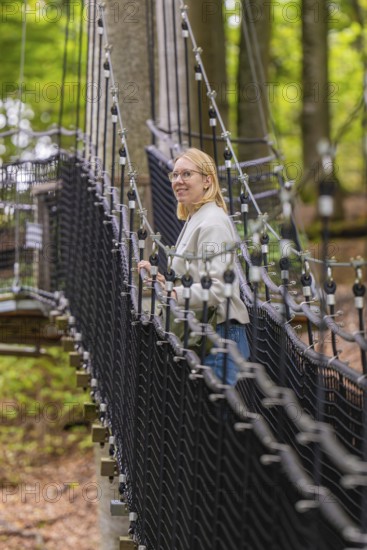 Woman on a rope bridge through a forest, Treewalk, Affenberg Salem, Bodenseekreis, Germany