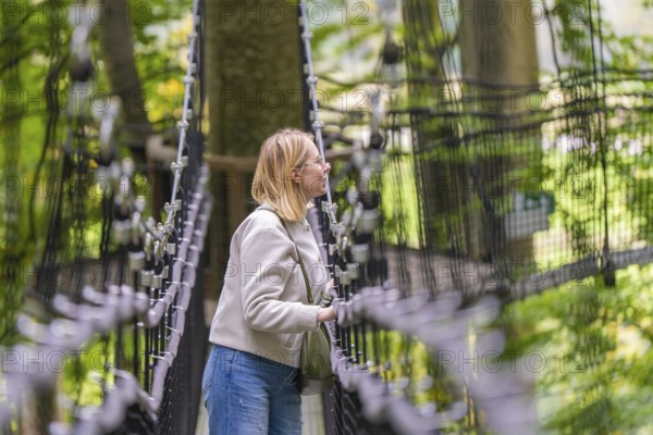 Woman on a rope bridge in the forest, surrounded by trees, Treewalk, Affenberg Salem, Bodenseekreis, Germany