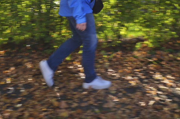 Person, woman, walks on sidewalk full of autumn leaves, autumn, leaves lying on sidewalk, movement effect, blurred, Stuttgart, Baden-Württemberg, Germany