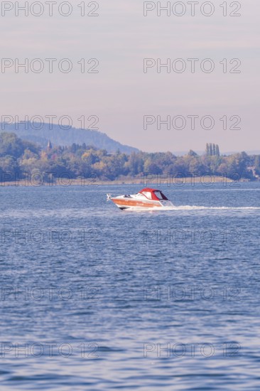 A motorboat sails at high speed across a quiet lake in autumn surroundings, boat trip, Lake Constance, Germany