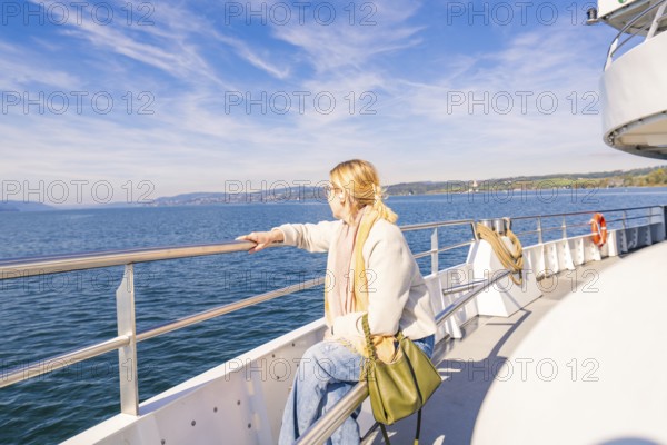 A woman stands relaxed at the railing of a ship and looks out to sea in sunny weather, Schiff Fahrt, Lake Constance, Germany